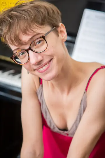 Slim Short-Haired Woman in Glasses Spreads on a Piano Bench