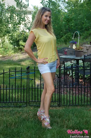 Kelly Anderson – Brunette MILF in Shorts and High Heels Shows Her Feet on Lush Grass